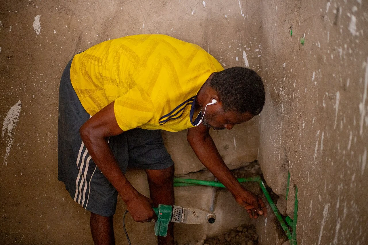 A plumber working on a water connection in an unfinished apartment